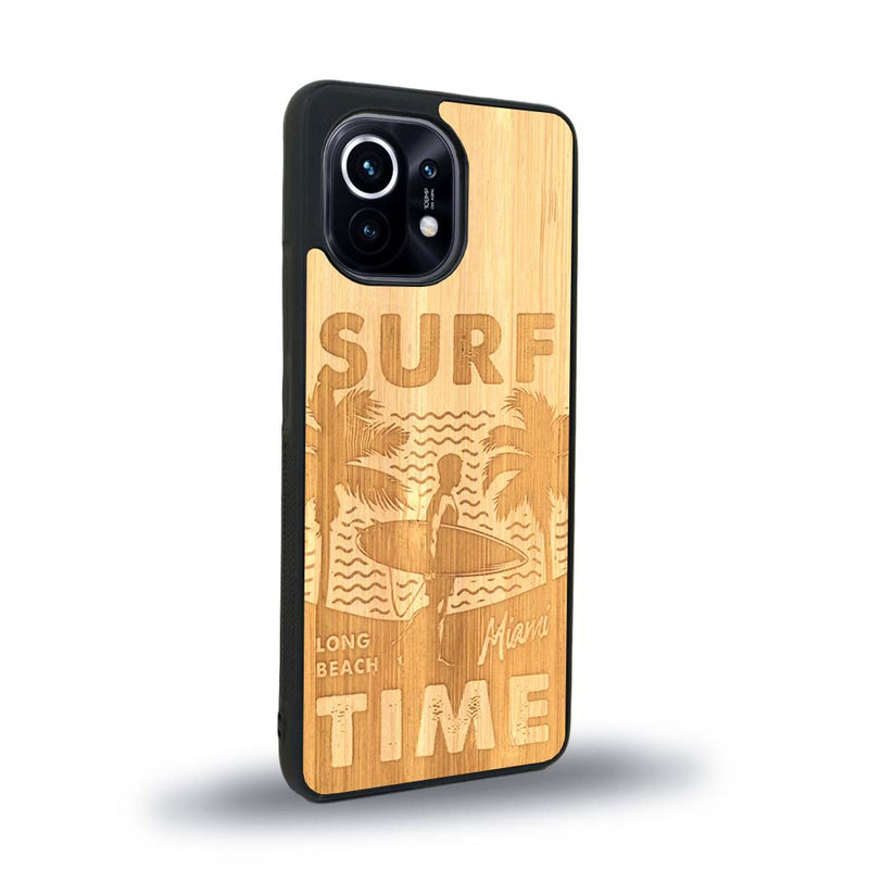 Coque de protection en bois véritable fabriquée en France pour Xiaomi Mi 11 Lite sur le thème chill avec un motif représentant une silouhette tenant une planche de surf sur une plage entouré de palmiers et les mots "Surf Time Long Beach Miami"