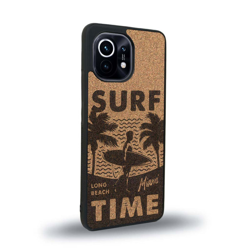 Coque de protection en bois véritable fabriquée en France pour Xiaomi Mi 11 Lite sur le thème chill avec un motif représentant une silouhette tenant une planche de surf sur une plage entouré de palmiers et les mots "Surf Time Long Beach Miami"