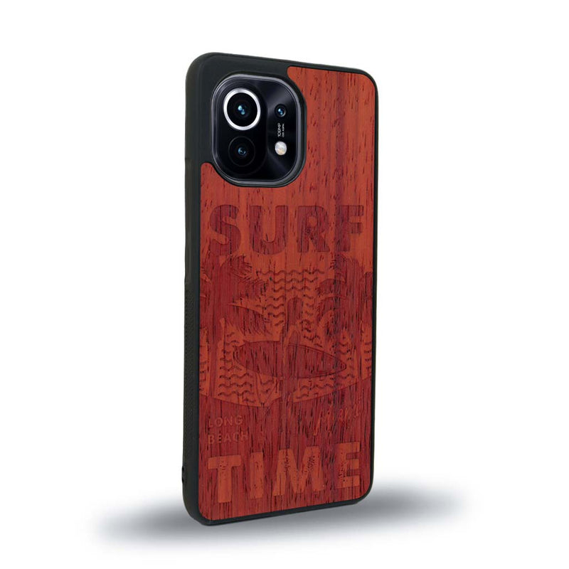 Coque de protection en bois véritable fabriquée en France pour Xiaomi Mi 11 Lite sur le thème chill avec un motif représentant une silouhette tenant une planche de surf sur une plage entouré de palmiers et les mots "Surf Time Long Beach Miami"