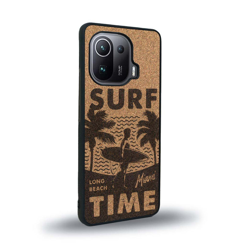 Coque de protection en bois véritable fabriquée en France pour Xiaomi Mi 11 Pro sur le thème chill avec un motif représentant une silouhette tenant une planche de surf sur une plage entouré de palmiers et les mots "Surf Time Long Beach Miami"