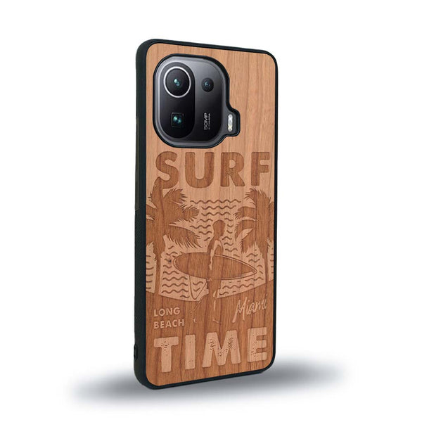 Coque de protection en bois véritable fabriquée en France pour Xiaomi Mi 11 Pro sur le thème chill avec un motif représentant une silouhette tenant une planche de surf sur une plage entouré de palmiers et les mots "Surf Time Long Beach Miami"