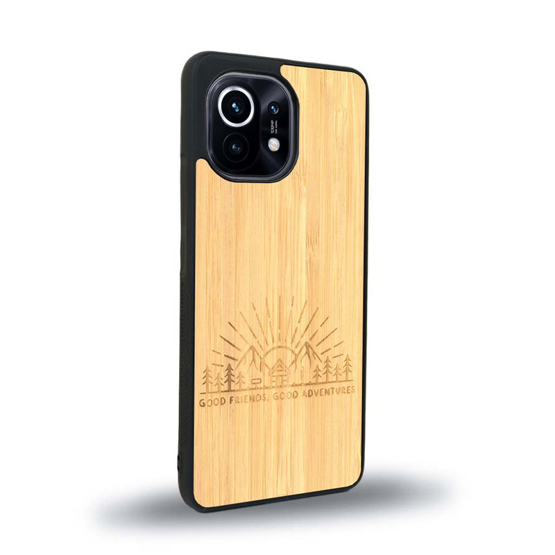 Coque de protection en bois véritable fabriquée en France pour Xiaomi Mi 11 sur le thème chill et nature avec un motif représentant un levé de soleil sur un paysage de montagne avec des sapins et un chalet et la phrase "Good friends, good adventure"