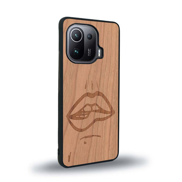 Coque de protection en bois véritable fabriquée en France pour Xiaomi Mi 11 Ultra représentant de manière minimaliste une bouche de féminine se mordant le coin de la lèvre de manière sensuelle dessinée à la main par l'artiste Maud Dabs