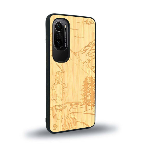 Coque de protection en bois véritable fabriquée en France pour Xiaomi Mi 11i sur le thème de la randonnée en montagne et de l'aventure avec une gravure représentant une femme de dos face à un paysage de nature