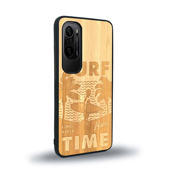 Coque de protection en bois véritable fabriquée en France pour Xiaomi Mi 11i sur le thème chill avec un motif représentant une silouhette tenant une planche de surf sur une plage entouré de palmiers et les mots "Surf Time Long Beach Miami"