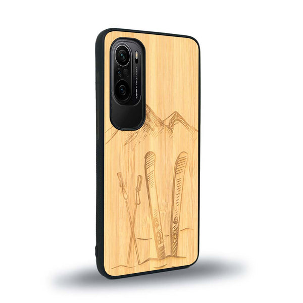 Coque de protection en bois véritable fabriquée en France pour Xiaomi Mi 11i sur le thème de la montagne, du ski et de la neige avec un motif représentant une paire de ski plantée dans la neige avec en fond des montagnes enneigées