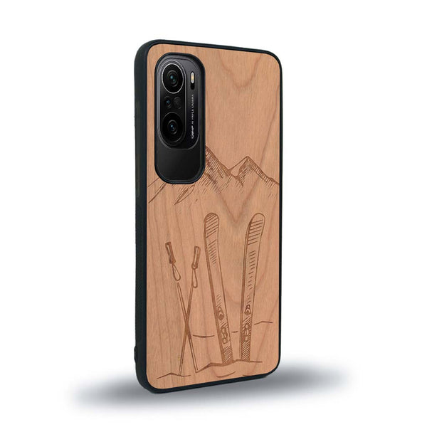 Coque de protection en bois véritable fabriquée en France pour Xiaomi Mi 11i sur le thème de la montagne, du ski et de la neige avec un motif représentant une paire de ski plantée dans la neige avec en fond des montagnes enneigées