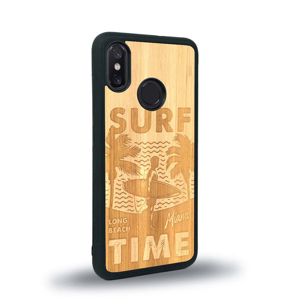 Coque de protection en bois véritable fabriquée en France pour Xiaomi Mi 8 sur le thème chill avec un motif représentant une silouhette tenant une planche de surf sur une plage entouré de palmiers et les mots "Surf Time Long Beach Miami"
