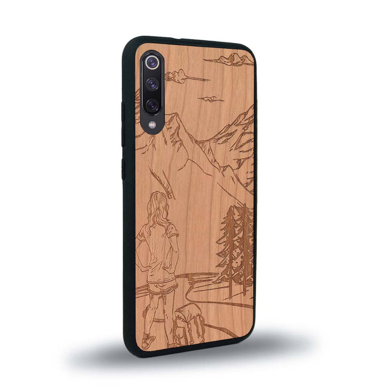 Coque de protection en bois véritable fabriquée en France pour Xiaomi Mi 9SE sur le thème de la randonnée en montagne et de l'aventure avec une gravure représentant une femme de dos face à un paysage de nature