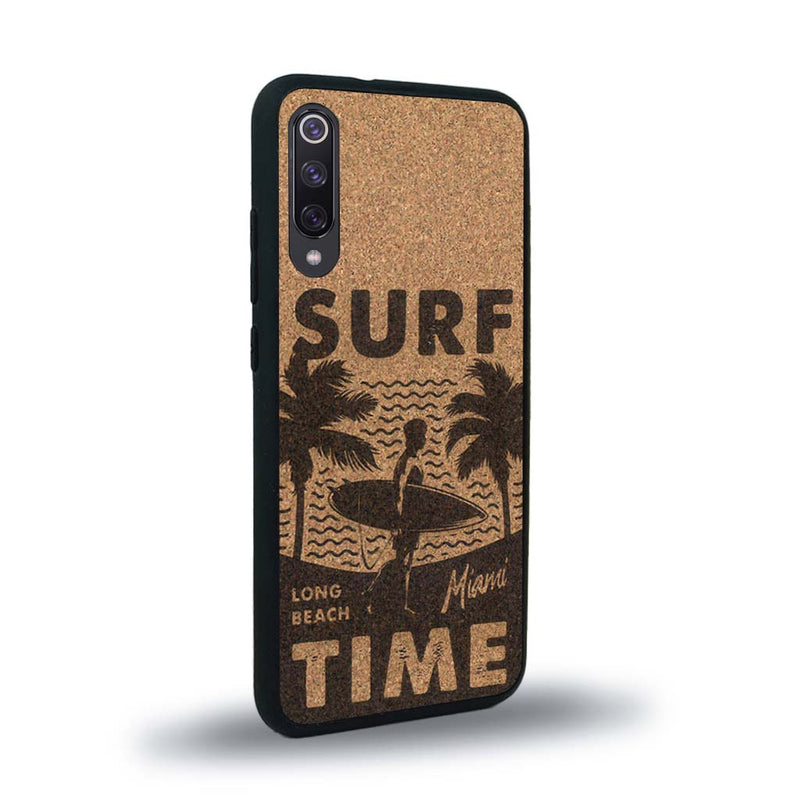 Coque de protection en bois véritable fabriquée en France pour Xiaomi Mi 9SE sur le thème chill avec un motif représentant une silouhette tenant une planche de surf sur une plage entouré de palmiers et les mots "Surf Time Long Beach Miami"