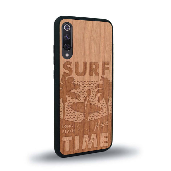 Coque de protection en bois véritable fabriquée en France pour Xiaomi Mi A3 sur le thème chill avec un motif représentant une silouhette tenant une planche de surf sur une plage entouré de palmiers et les mots "Surf Time Long Beach Miami"