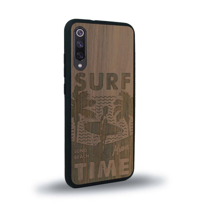 Coque de protection en bois véritable fabriquée en France pour Xiaomi Mi A3 sur le thème chill avec un motif représentant une silouhette tenant une planche de surf sur une plage entouré de palmiers et les mots "Surf Time Long Beach Miami"