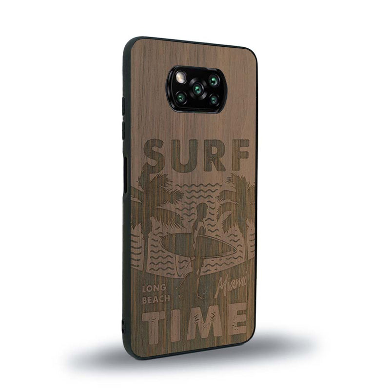 Coque de protection en bois véritable fabriquée en France pour Xiaomi Poco X3 Nfc sur le thème chill avec un motif représentant une silouhette tenant une planche de surf sur une plage entouré de palmiers et les mots "Surf Time Long Beach Miami"