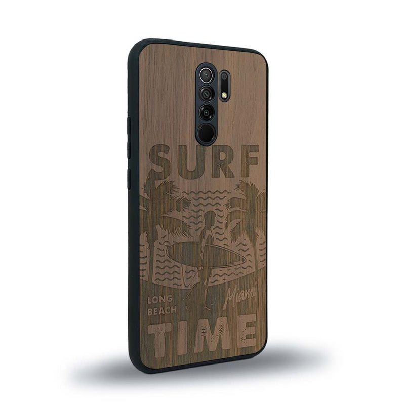 Coque de protection en bois véritable fabriquée en France pour Xiaomi Redmi 9 sur le thème chill avec un motif représentant une silouhette tenant une planche de surf sur une plage entouré de palmiers et les mots "Surf Time Long Beach Miami"